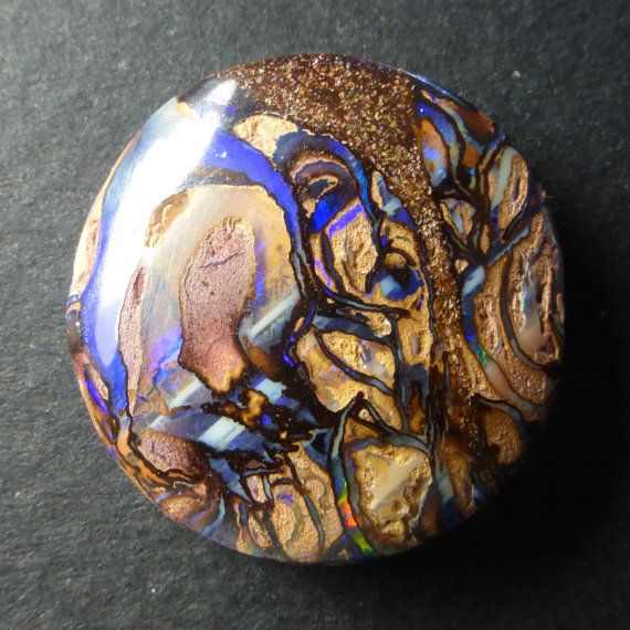 a close up of a rock on a black surface with gold and blue paint splatters