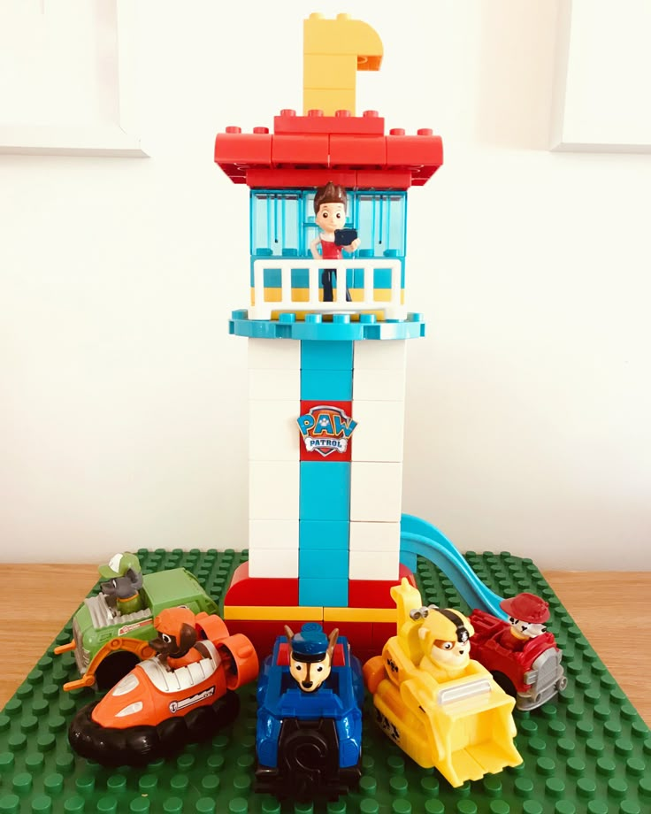 a lego toy tower with cars and a person in it on a table next to a window