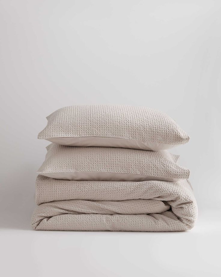 three linen pillows stacked on top of each other in front of a white wall and floor