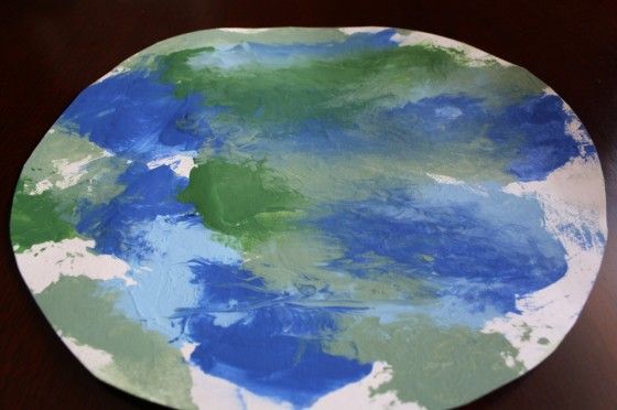 a plate with blue, green and white paint on it sitting on a wooden table