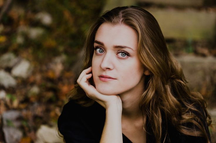 a woman with long brown hair and blue eyes is looking at the camera while leaning on her hand