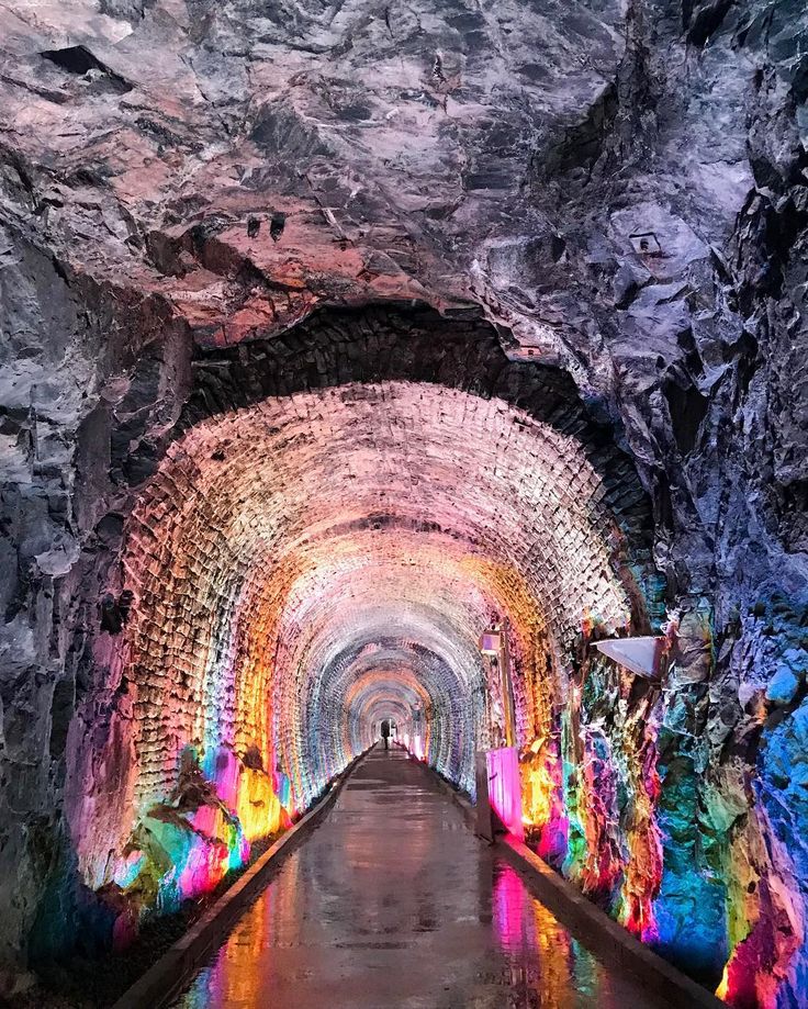 a long tunnel filled with lots of colorful lights next to a walkway in the middle of a cave