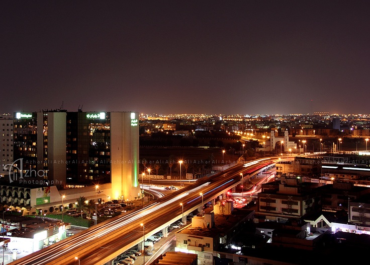 an aerial view of a city at night with lights and buildings in the foreground