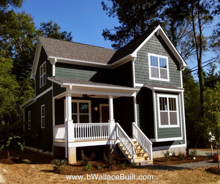 a small gray and white house in the woods with stairs leading up to it's front door