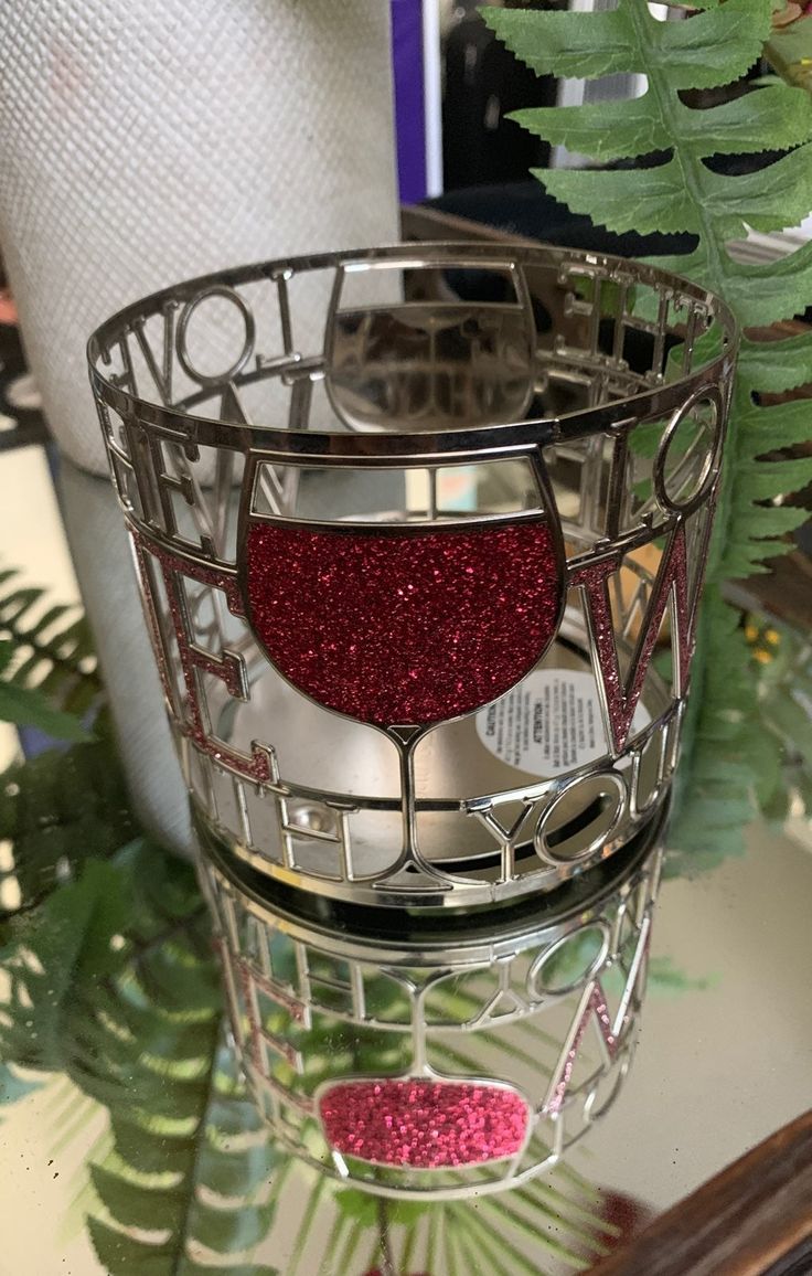 a metal container with red glitter on the top and bottom, sitting next to a green plant