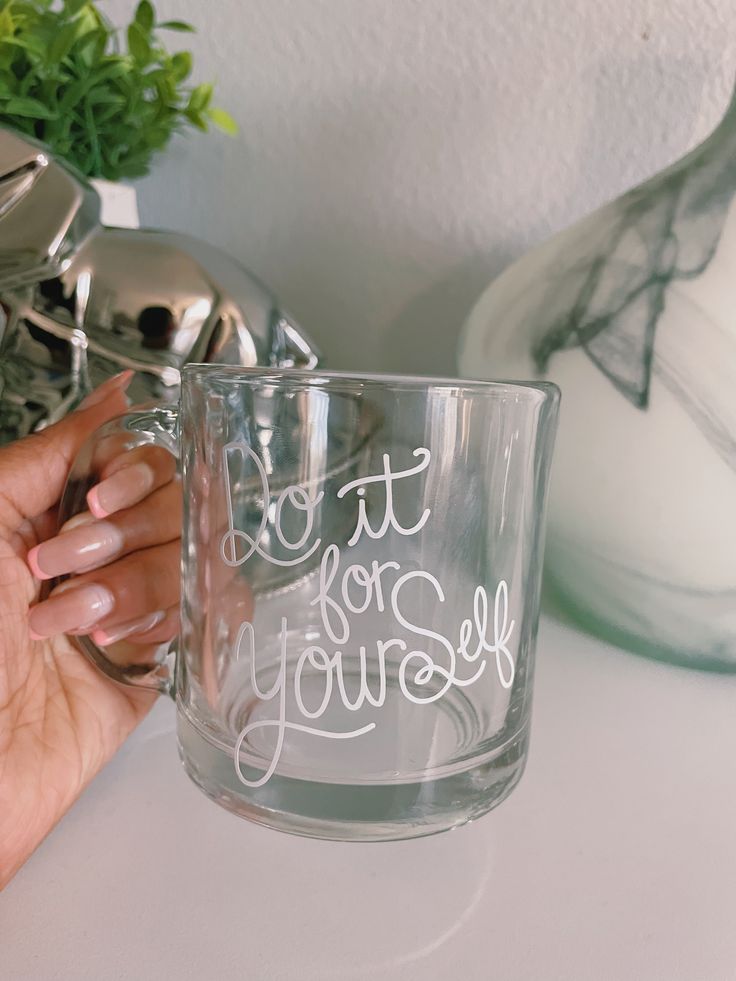 a person holding a glass mug with writing on it