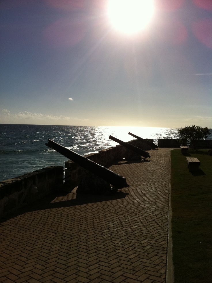 the sun shines brightly over an ocean wall with benches on it and water in the background