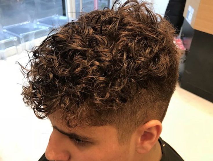 a young man with curly hair in a barbershop looking down at his phone