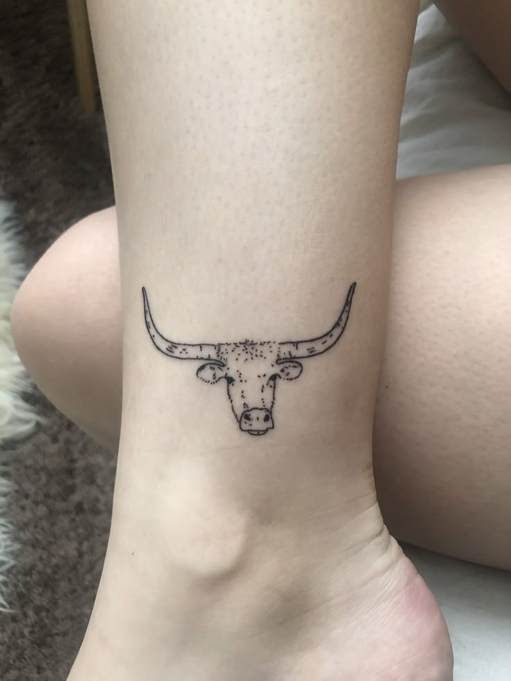 a woman's foot with a tattoo of a bull head on the side of her leg