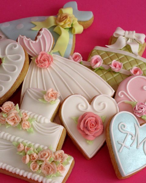 decorated cookies are arranged in the shape of wedding dresses and groom's shoes on a pink background