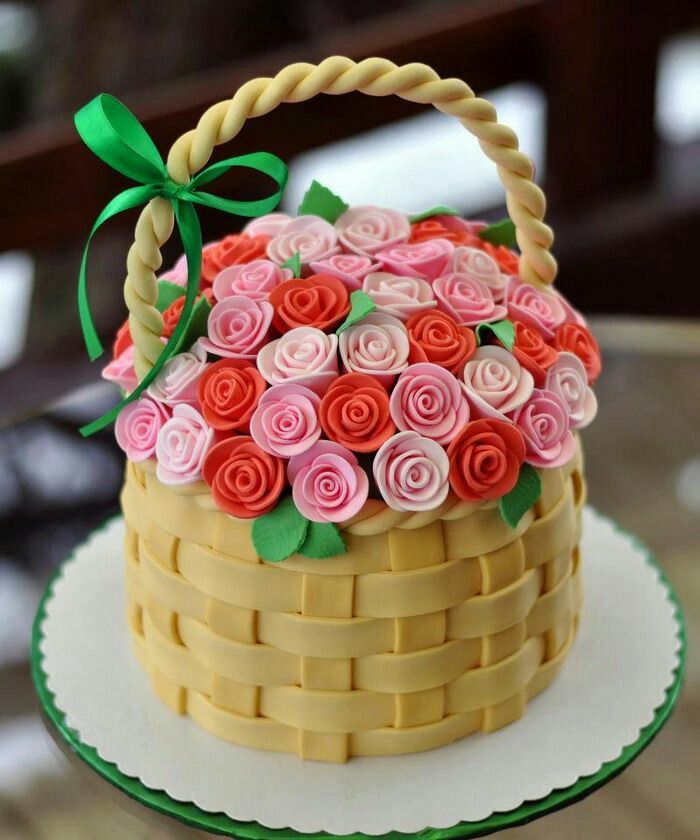 a cake decorated with pink and red flowers in a basket on a plate, sitting on a table