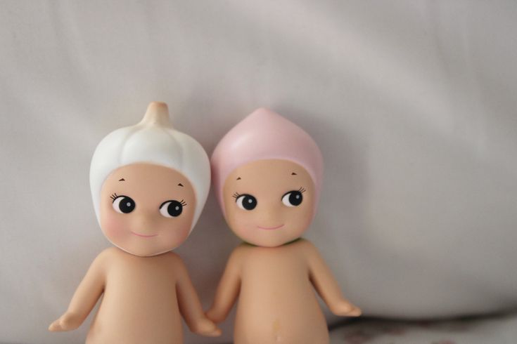 two small dolls sitting next to each other on top of a white sheet covered bed