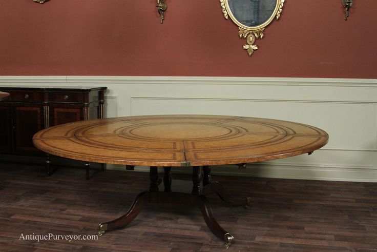 an oval wooden table with two mirrors on the wall behind it in a room with wood flooring and red walls