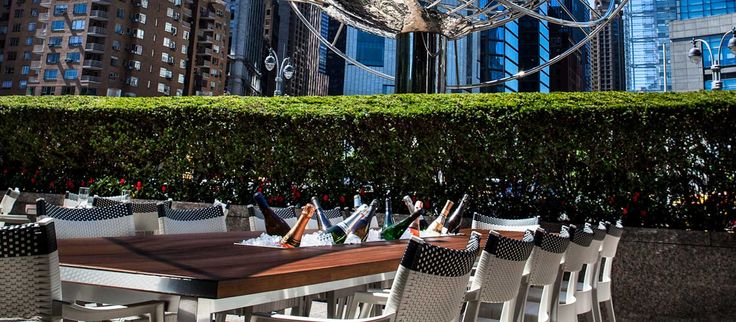 an outdoor dining area with tables and chairs in the foreground, surrounded by tall buildings