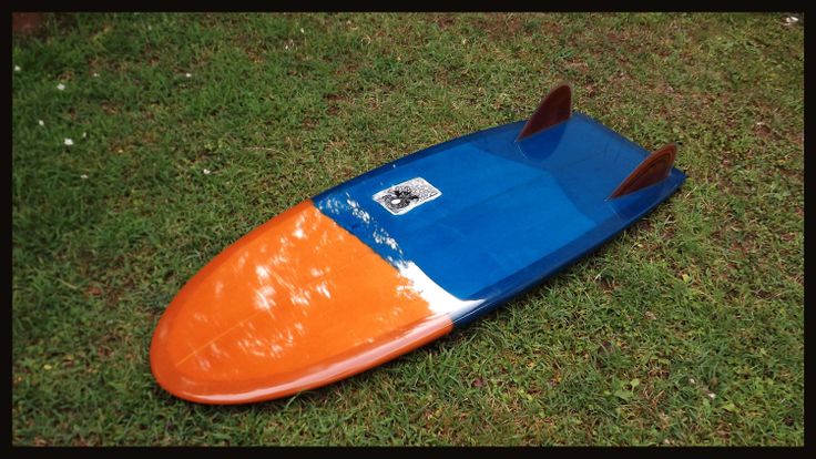 an orange and blue surfboard laying on the ground in the grass with it's fins sticking out