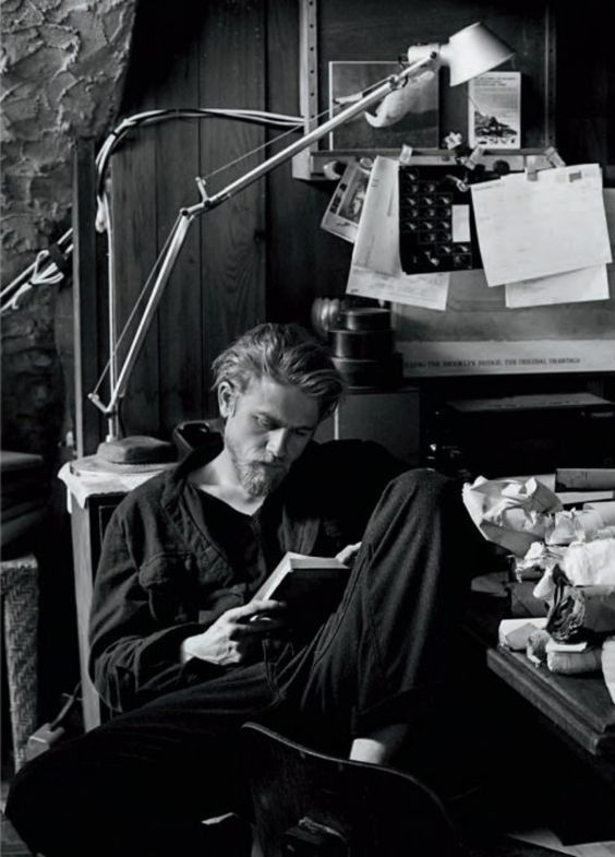 a man sitting on the floor in front of a desk with papers and a lamp