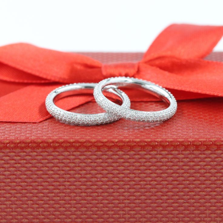 two wedding rings sitting on top of a red gift box with a ribbon around it