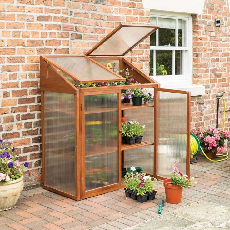 a small greenhouse with plants in it on the side of a brick wall next to a potted planter