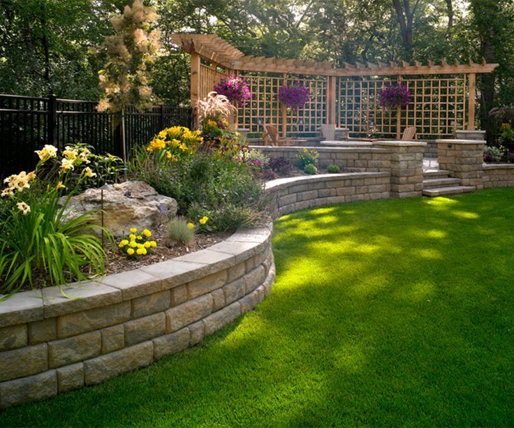 an outdoor garden with grass and flowers on the ground, surrounded by stone retaining walls