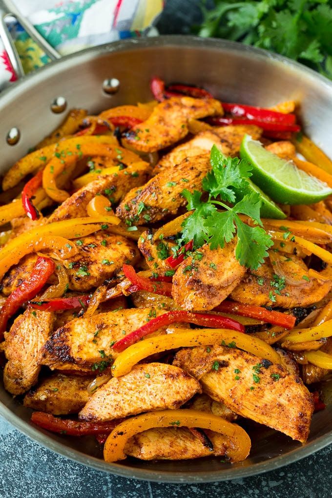 a pan filled with chicken, peppers and cilantro on top of a table