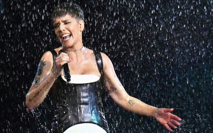 a woman singing in the rain with her hands out to her side while holding an umbrella