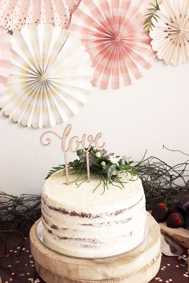 a white cake sitting on top of a wooden table next to paper fans and flowers