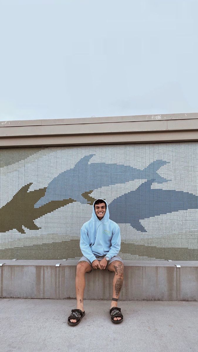 a man sitting on a bench in front of a wall with dolphins painted on it