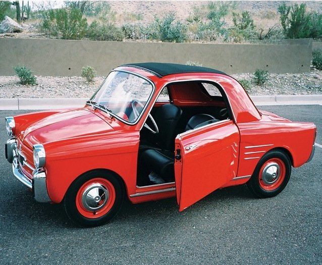 an old red car parked in a parking lot with its door open and the driver's seat up