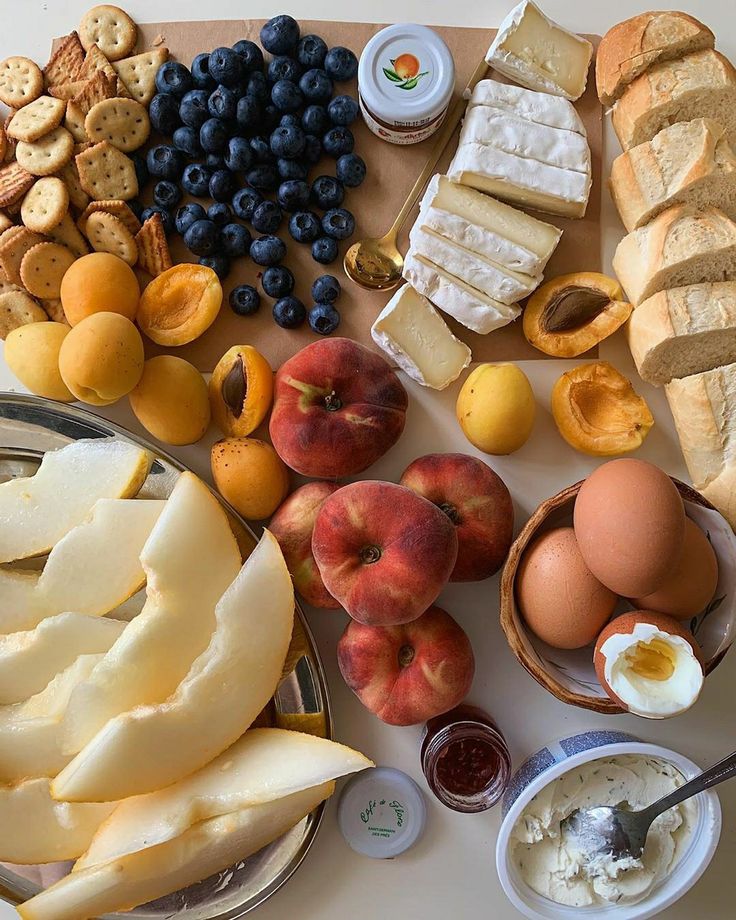 an assortment of cheeses, fruit and crackers on a cutting board with butter