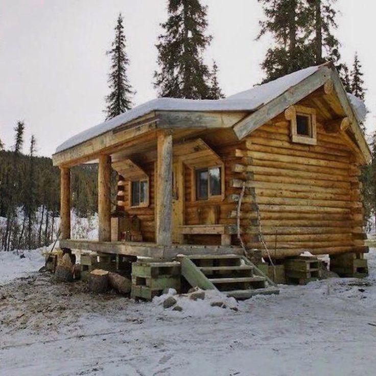 a small log cabin in the snow with stairs leading up to it's roof