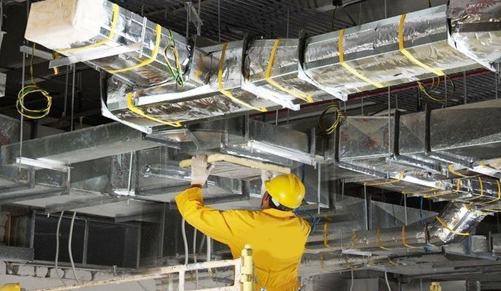 a man in yellow jacket and safety gear working on an overhead fixture with wires attached to the ceiling