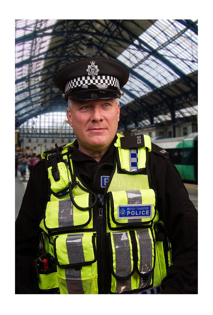 a police officer is standing in front of a train station with his hand on his hip