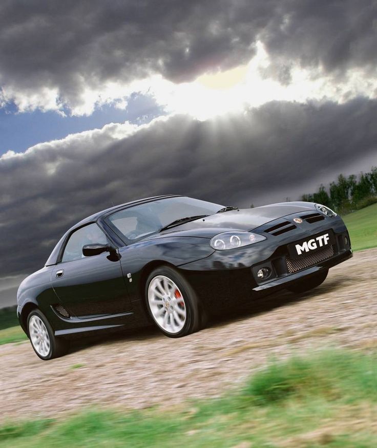 a black sports car driving down a dirt road under a cloudy sky with trees in the background