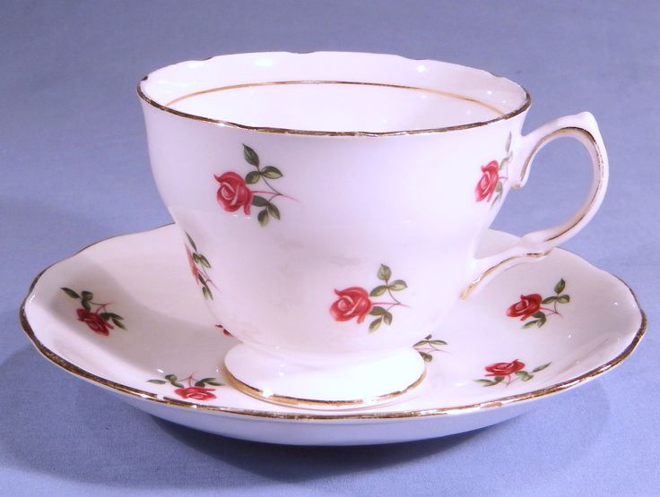 a tea cup and saucer with red roses on the rim, against a blue background