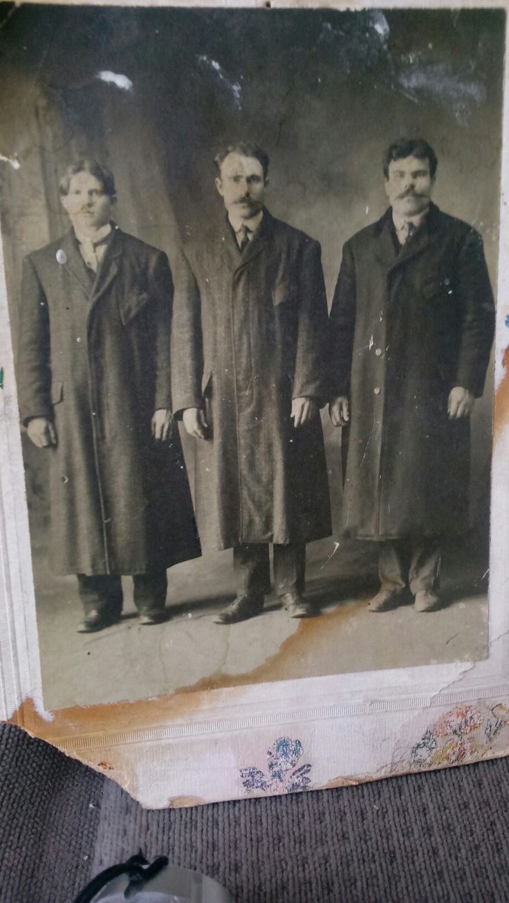 an old black and white photo of three men in long coats standing next to each other