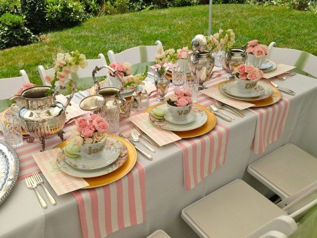 a table set with plates, silverware and pink flowers on it in the backyard