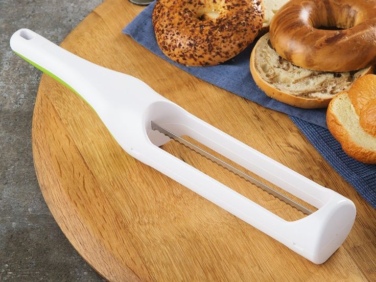 a cutting board with bread, bagels and jams on it next to a knife