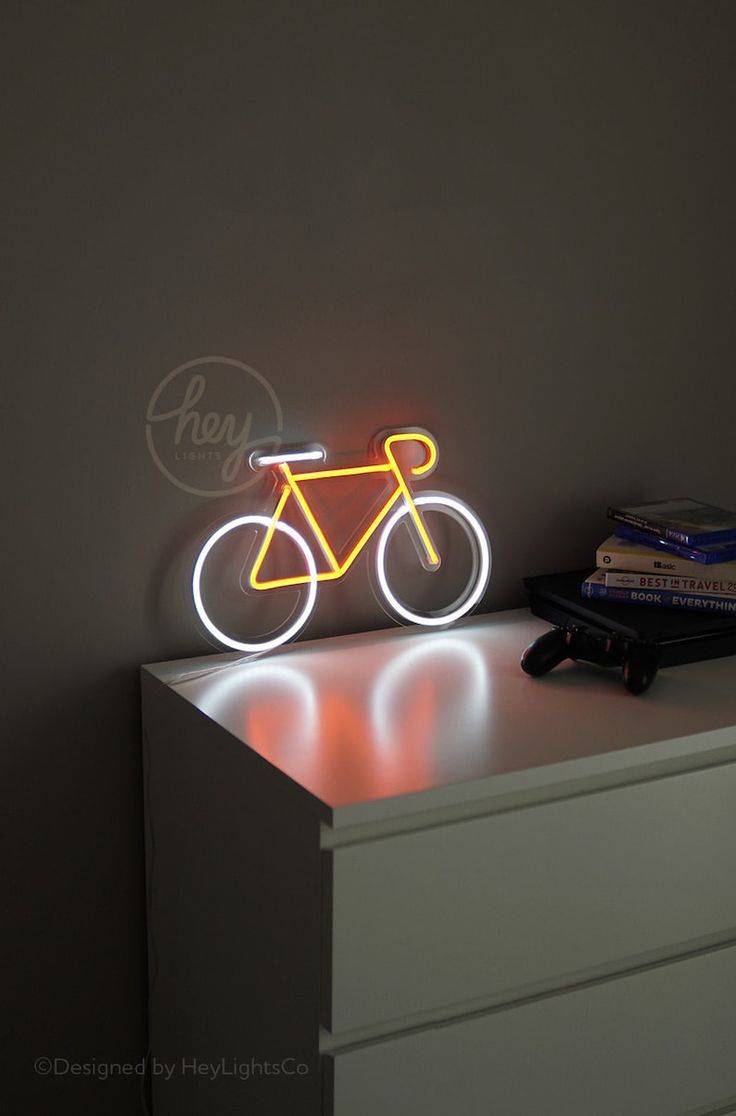 a neon bicycle sign sitting on top of a dresser next to a stack of books