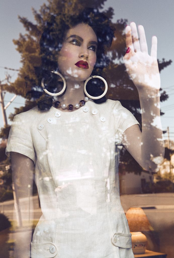 a woman is standing in front of a window with her hand up to the sky