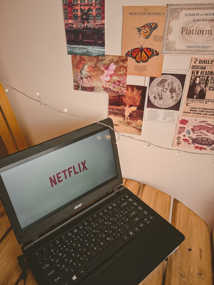 a laptop computer sitting on top of a wooden table next to a wall covered in posters