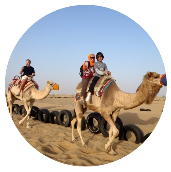 three people riding on top of two camels in the desert