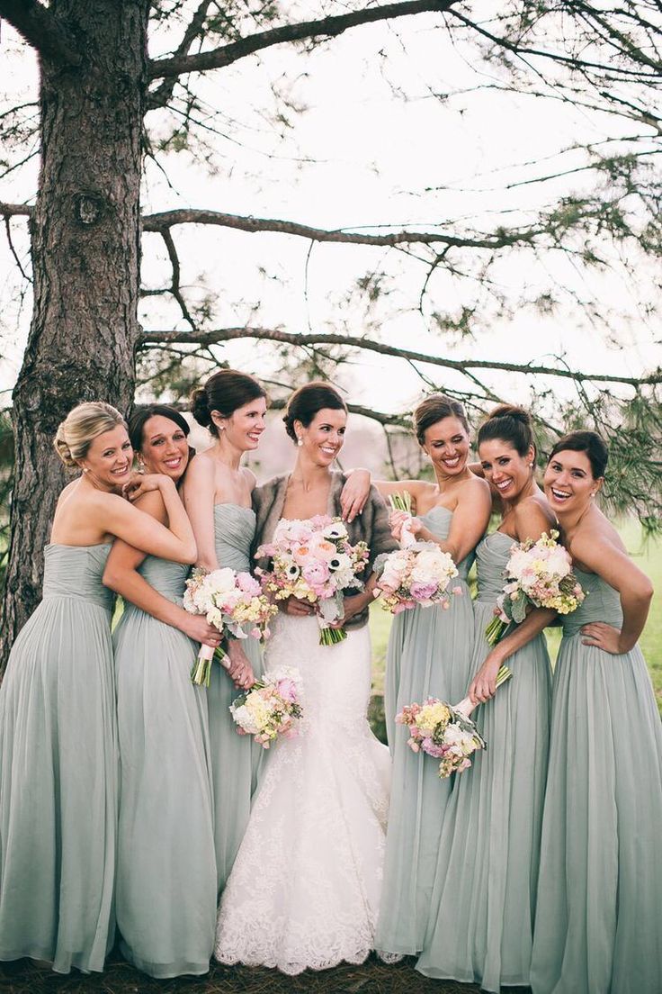 a group of women standing next to each other in front of a tree holding bouquets