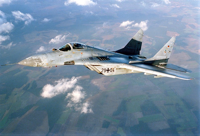 a fighter jet flying through the air over land and clouds in front of a blue sky