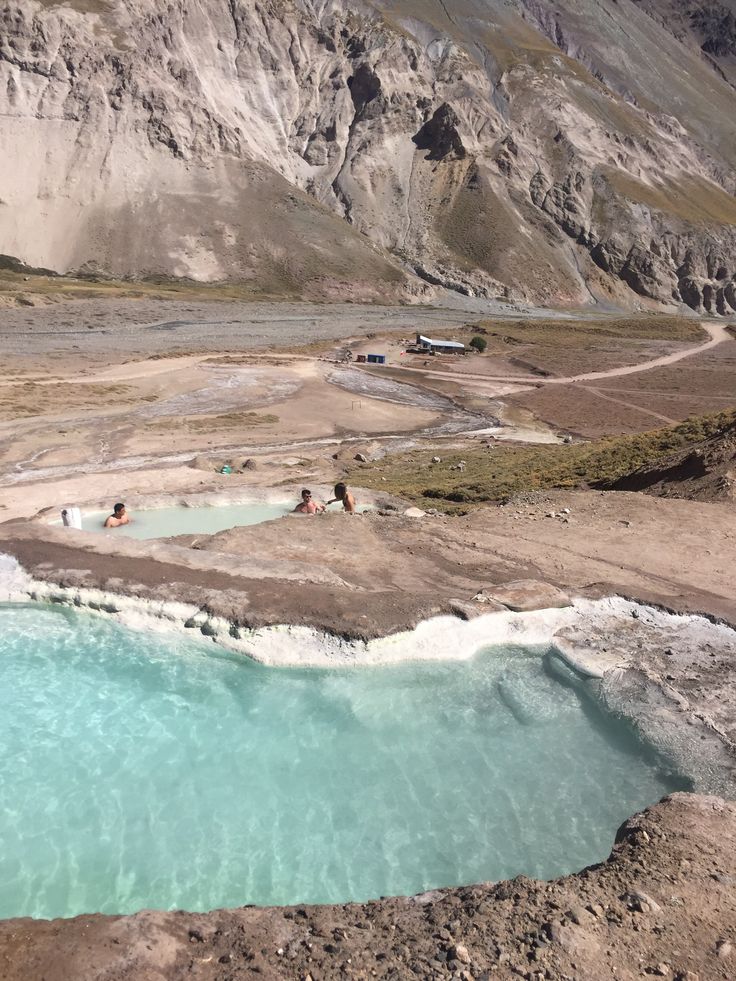 some people are swimming in the blue water at this mountain top area with mountains in the background