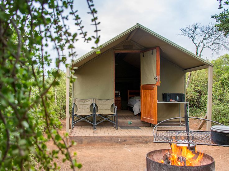 a small tent with a fire pit in the foreground and chairs on the other side