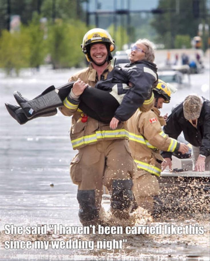 two firemen carrying a woman in a boat through flood waters