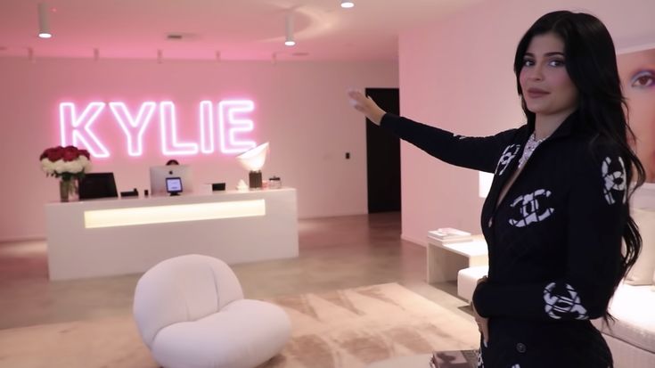 a woman standing in front of a living room filled with white furniture and pink lighting