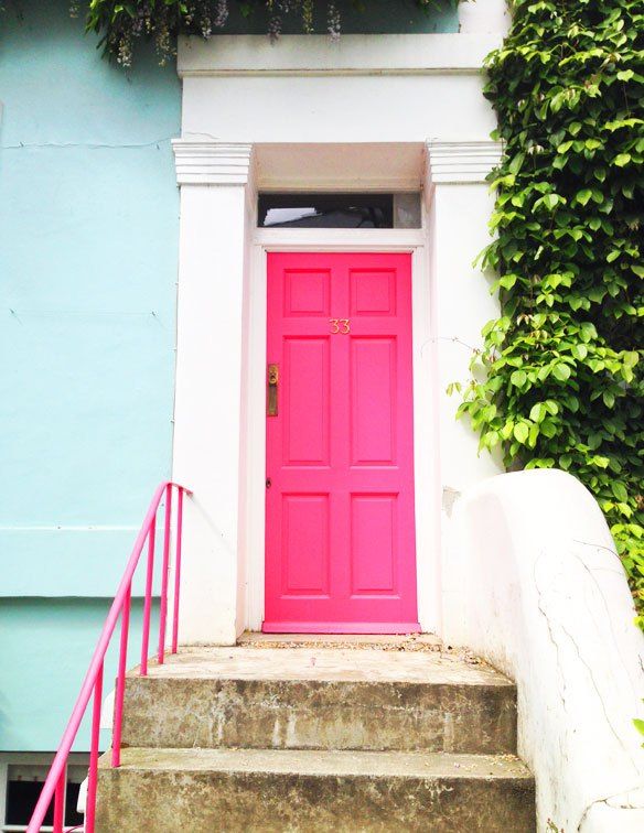 a bright pink door sits in front of a blue and white building with ivy growing on it