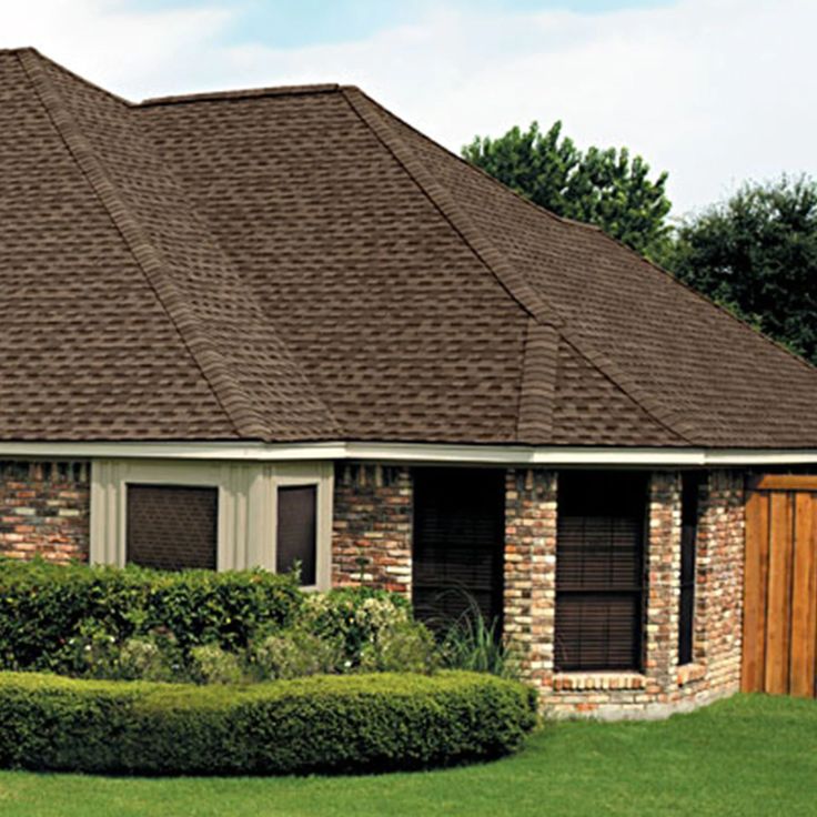 a house with brown shingles and hedges in the front yard