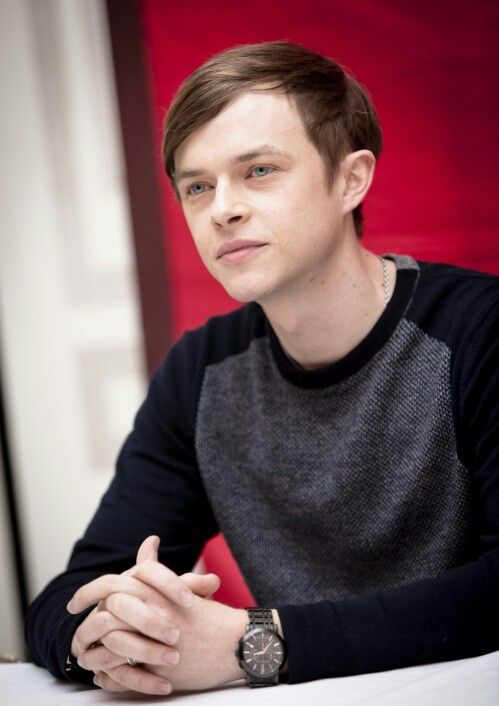 a young man sitting at a table with his hands folded in front of the camera